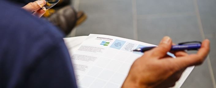 Person betrachtet Kompetenzrahmen von aufZAQ mit Brille und Stift in der Hand.