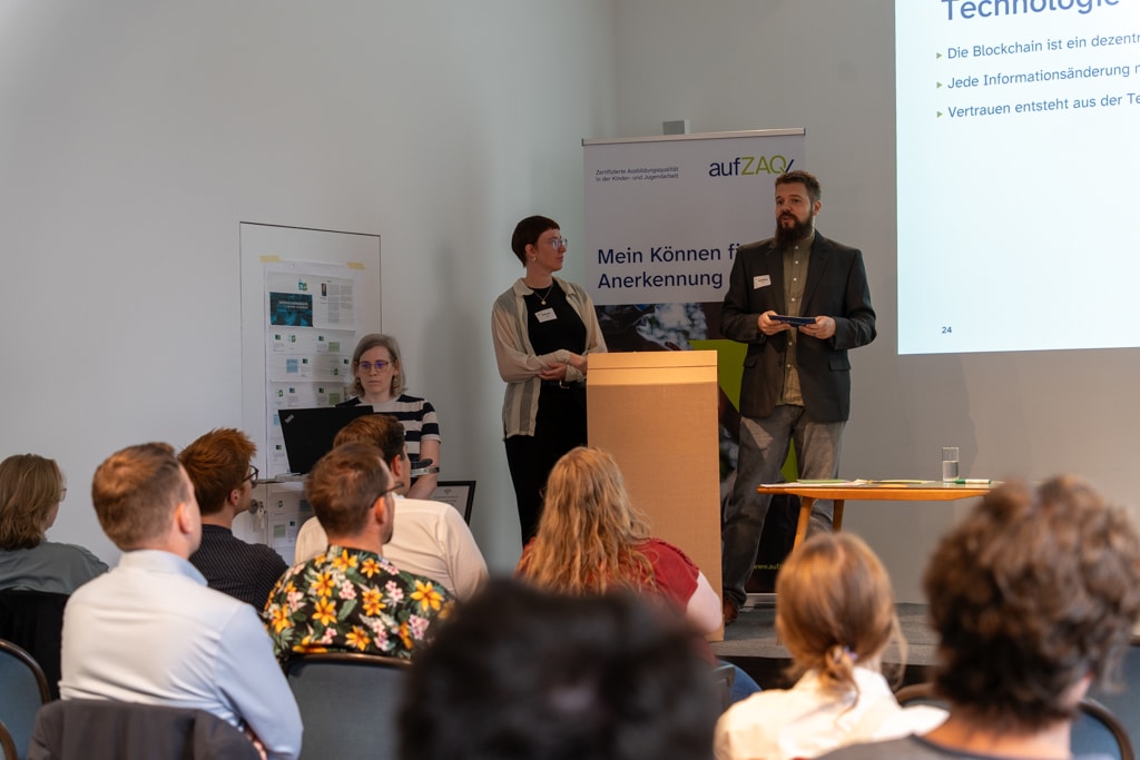 Zwei Personen präsentieren vor Publikum beim aufZAQ Impuls.Brunch. Banner im Hintergrund.