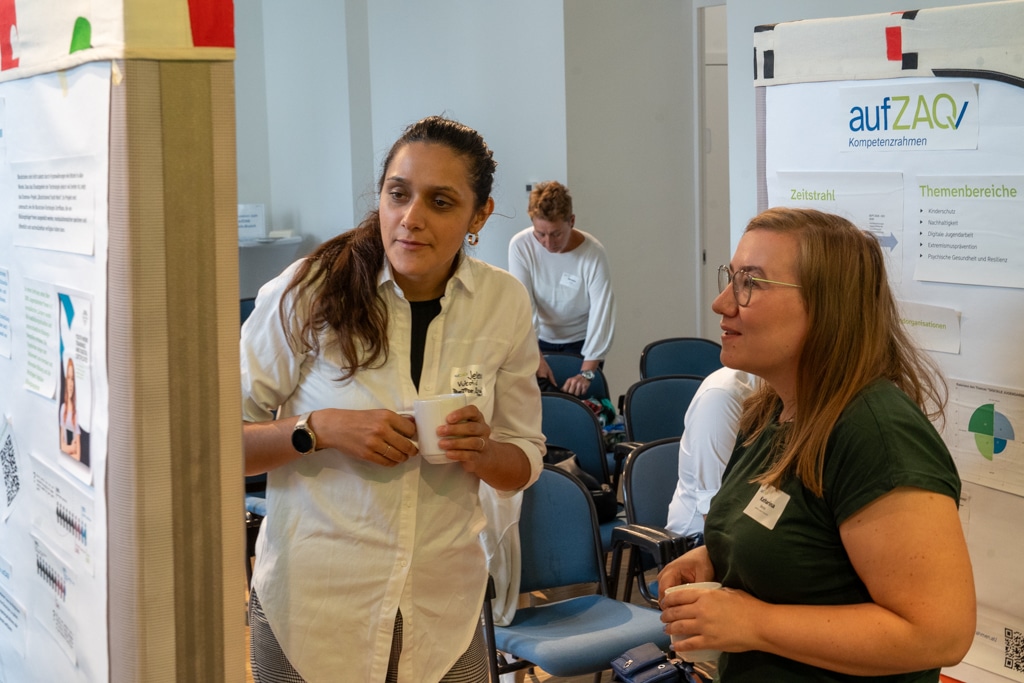 Zwei Frauen unterhalten sich beim aufZAQ Impuls.Brunch, Poster im Hintergrund.