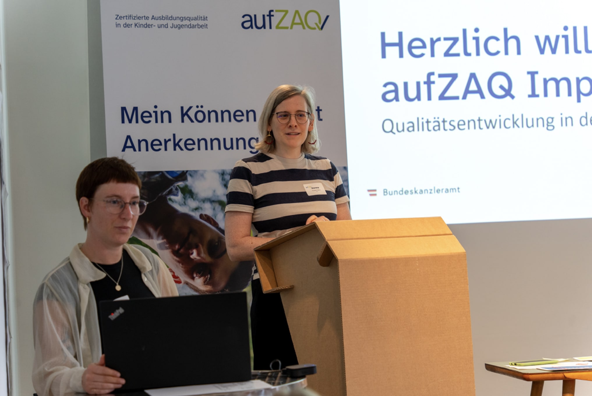 Frau hält Vortrag bei aufZAQ Veranstaltung zur Jugendarbeit. Kollegin mit Laptop.